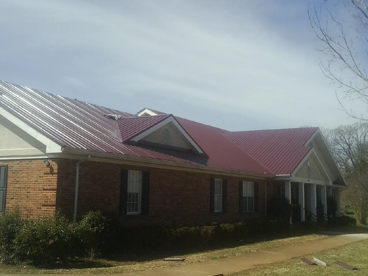 Red metal roof with gabled entries on a long brick building, from a Hail Damage Roof Repair job in Peekskill