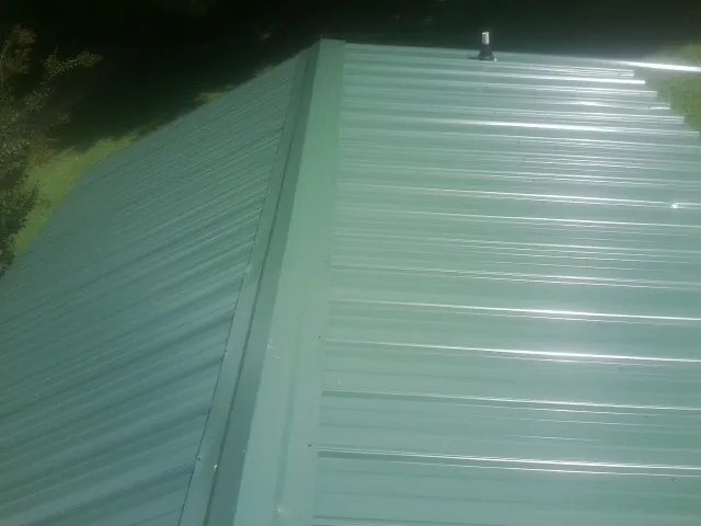 New green metal panels meeting at the ridge of a roof — Flat Roof Repair work by our crew in Peekskill