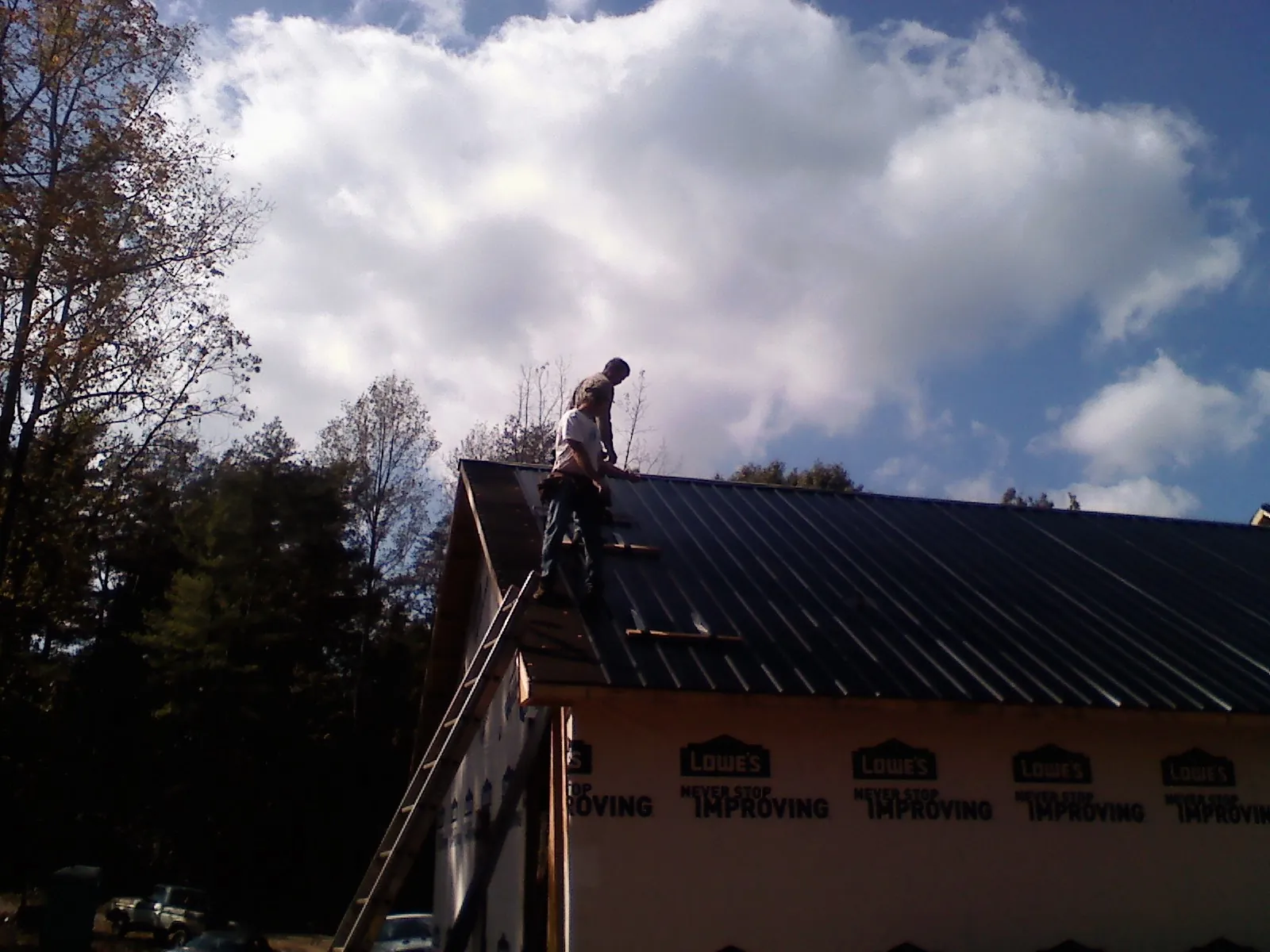Roofer fastening dark metal panels high against a cloudy sky, from a Roof Inspection job in Peekskill